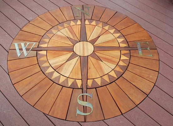 Compass design on wooden deck, featuring cardinal directions N, E, S, W, showcasing craftsmanship in outdoor living spaces.