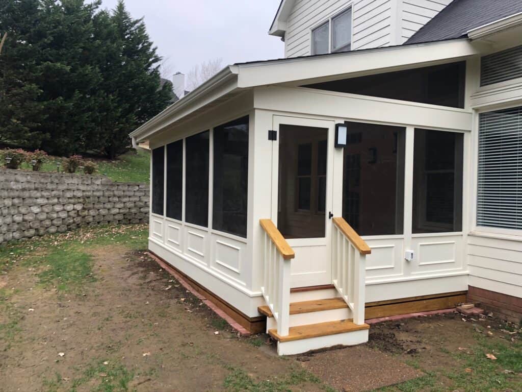 Custom outdoor screened porch with wooden steps, designed for enhanced outdoor living, surrounded by landscaped yard and stone wall, showcasing DW Construction's craftsmanship in Nashville, TN.