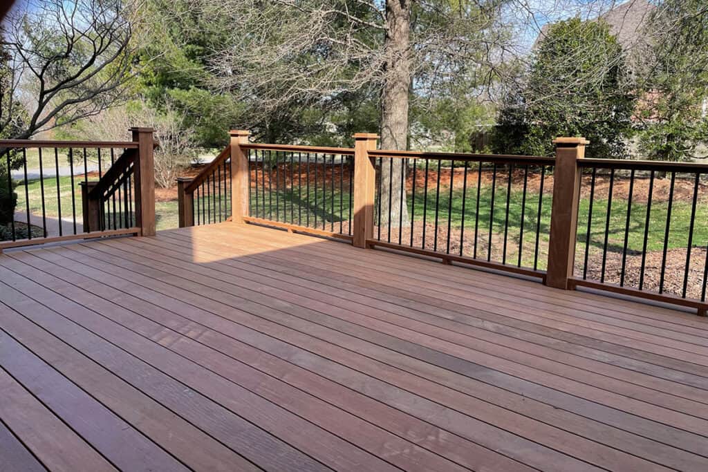 Custom wooden deck with black railing, surrounded by greenery, showcasing outdoor living space design inspiration for Nashville homes.