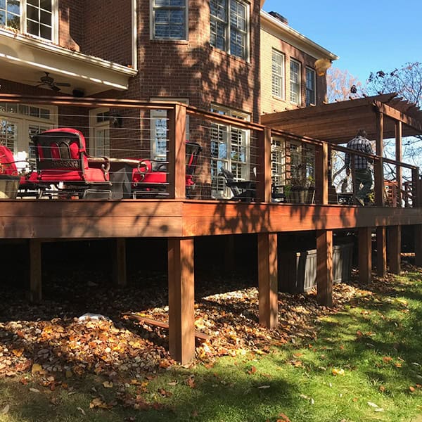 Custom wooden deck with red outdoor chairs, attached to a brick home, featuring a pergola and surrounded by autumn leaves in Nashville, TN.