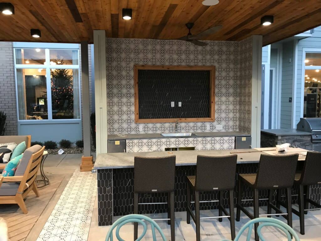 Outdoor kitchen bar area featuring a built-in countertop, stylish tile backsplash, and seating under a wooden pergola, designed for entertaining in a sophisticated outdoor living space.