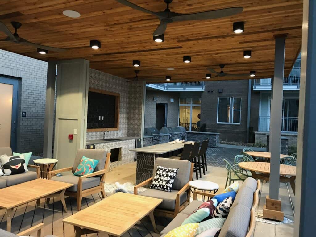 Outdoor living space featuring a wooden pergola with ceiling fans, stylish seating areas, and a built-in bar, designed for entertaining and relaxation in a modern setting.