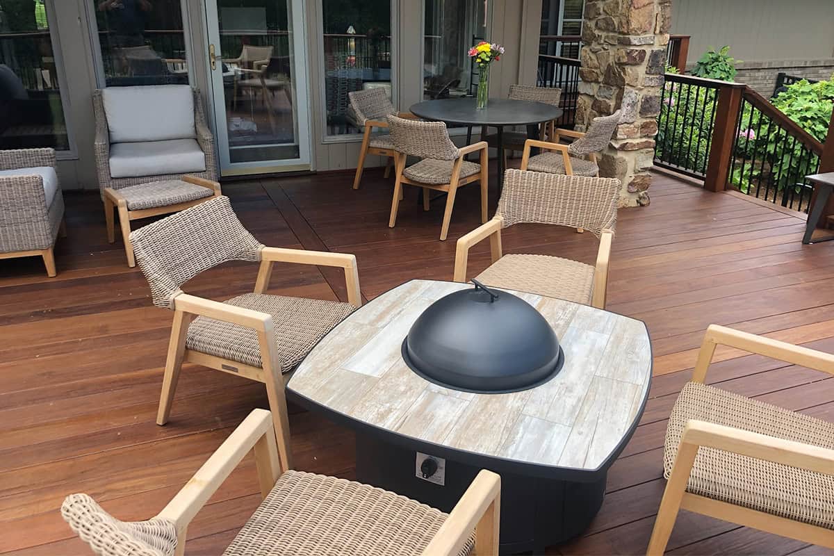 custom outdoor fire features 6 Modern outdoor seating arrangement with a central fire table, featuring a sleek black fire bowl, surrounded by woven chairs, enhancing outdoor living space ambiance.