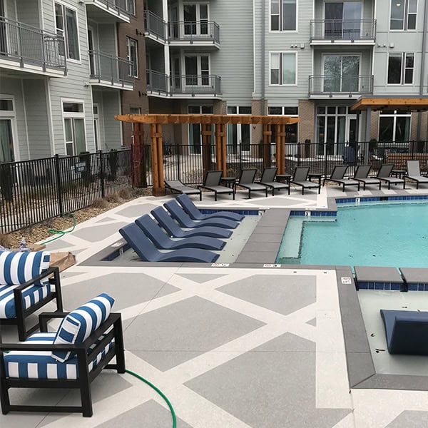Custom patio area with modern lounge chairs and a swimming pool, featuring a geometric design and outdoor pergola, enhancing outdoor living space for relaxation and entertainment.