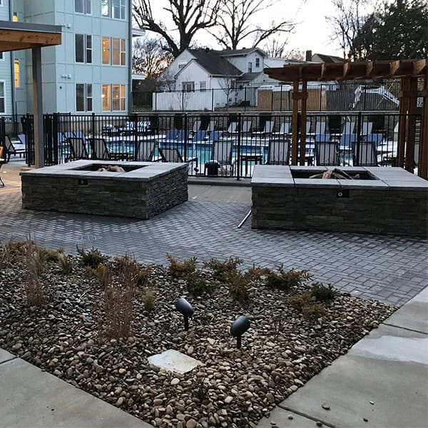Custom stone fire pits surrounded by landscaped gravel and plants, featuring a modern patio area with seating near a swimming pool, reflecting outdoor living design by DW Construction in Nashville, TN.