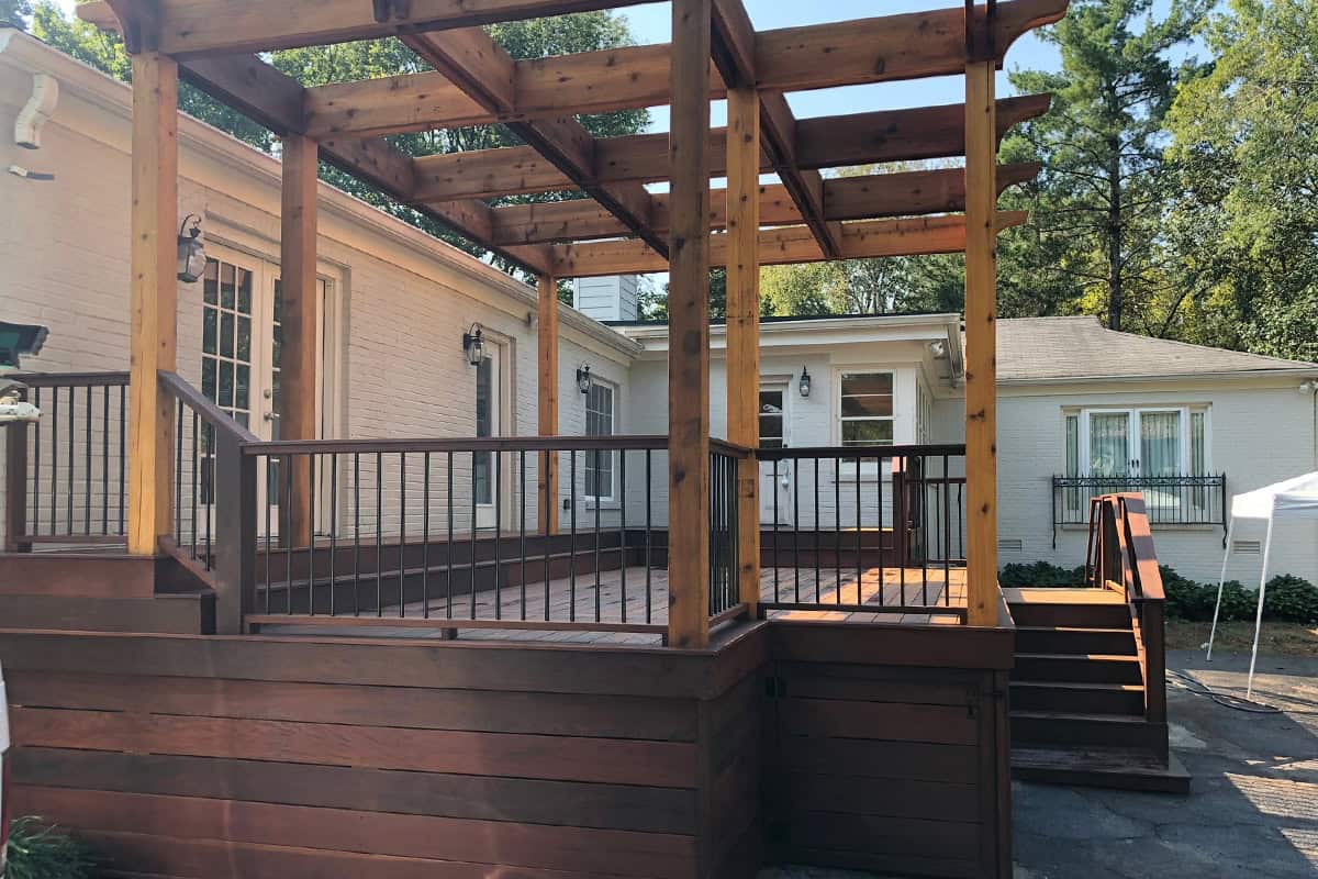 Custom wooden pergola over a spacious deck, enhancing outdoor living space, with access stairs and adjacent home entrance, showcasing architectural design for shade and aesthetic appeal.