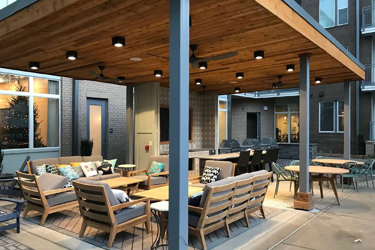 Modern outdoor living space featuring a covered aluminum pergola with wooden ceiling, comfortable seating area with decorative pillows, and dining tables, emphasizing stylish design and functionality for Nashville homeowners.
