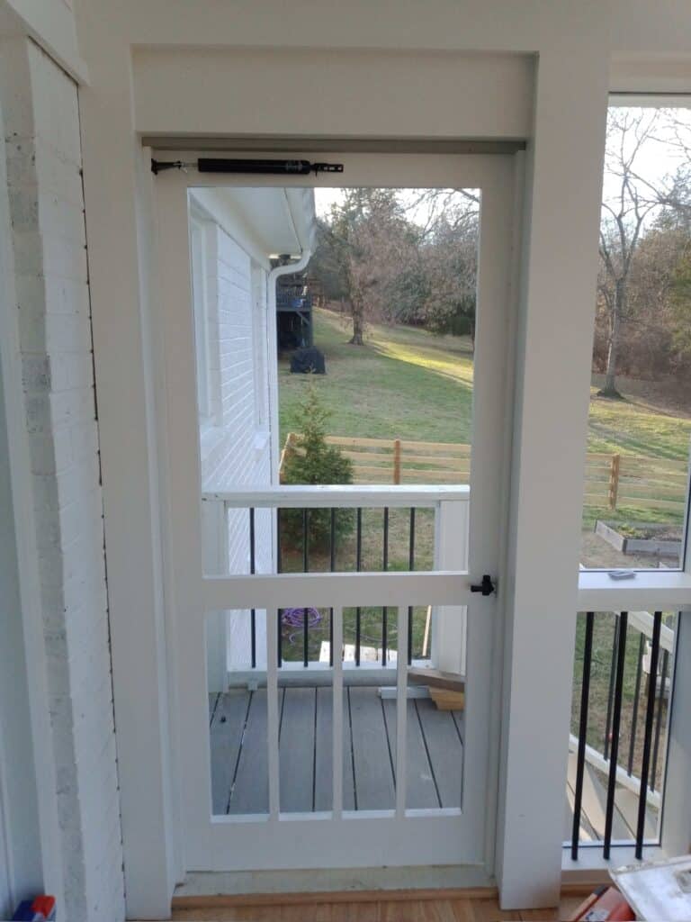 White wooden door leading to an outdoor space, showcasing a view of a grassy yard and wooden fence, emphasizing outdoor living design by DW Construction.