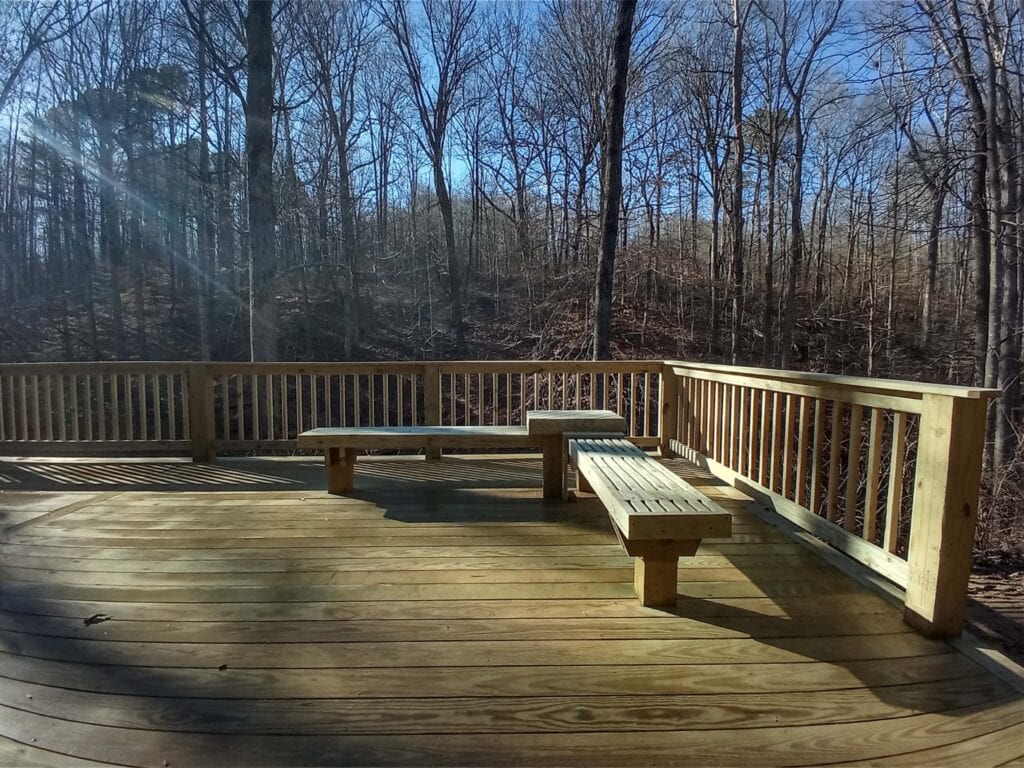 Wooden deck with built-in benches overlooking a wooded area, showcasing outdoor living space design by DW Construction.