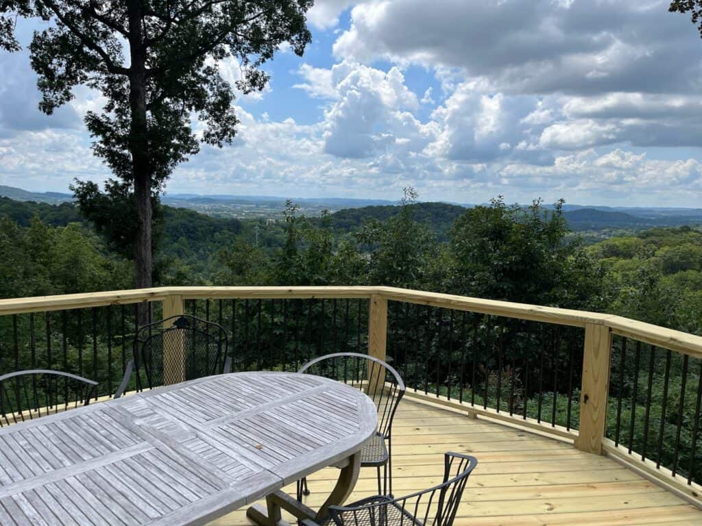 Deck with a wooden table and black chairs overlooking a scenic view of hills and clouds, showcasing outdoor living space designed by DW Construction.