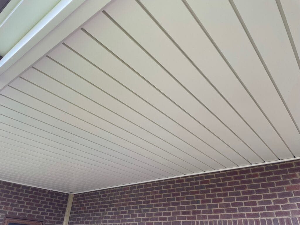Ceiling of a covered outdoor space featuring a clean, white panel design and brick wall background, showcasing the quality craftsmanship of DW Construction's outdoor living projects.