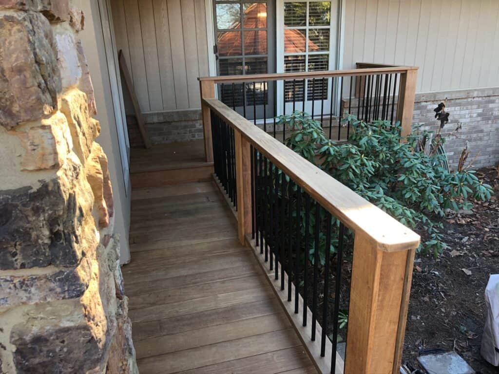 Wooden deck with black metal railing leading to a home entrance, surrounded by greenery, showcasing outdoor living design by DW Construction in Nashville.