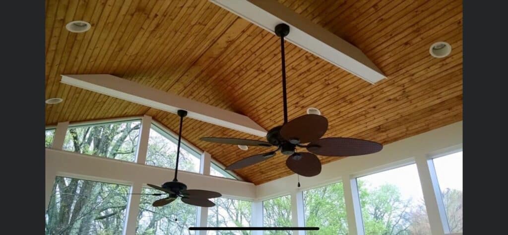 Ceiling with wooden beams and modern ceiling fans in a bright, airy sunroom showcasing outdoor living design elements.