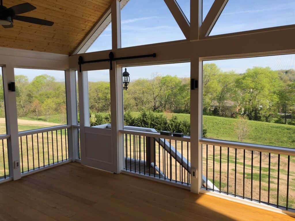 Spacious outdoor living space with wooden flooring, large windows showcasing green landscape, and modern railing design, highlighting DW Construction's custom porch design.