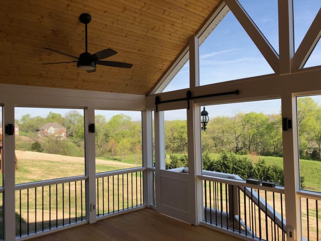 Spacious screened porch with wooden ceiling, ceiling fan, and panoramic views of green landscape, showcasing outdoor living design by DW Construction.