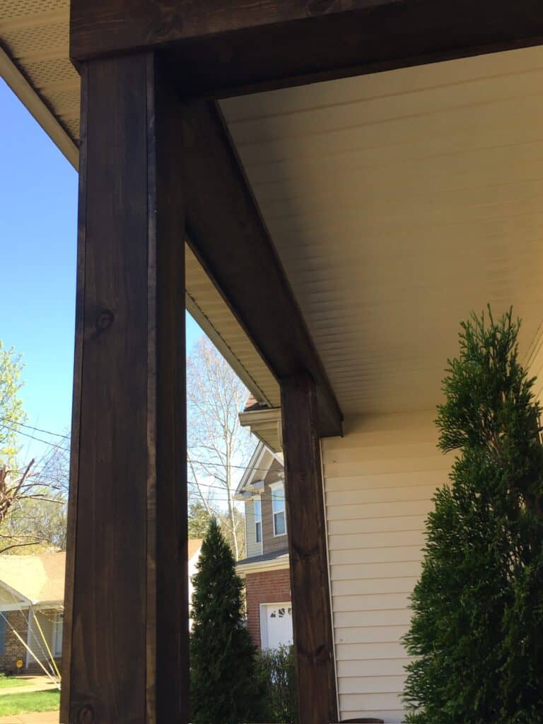 Wooden porch post and ceiling detail showcasing craftsmanship in outdoor living design by DW Construction, with nearby greenery and residential backdrop.