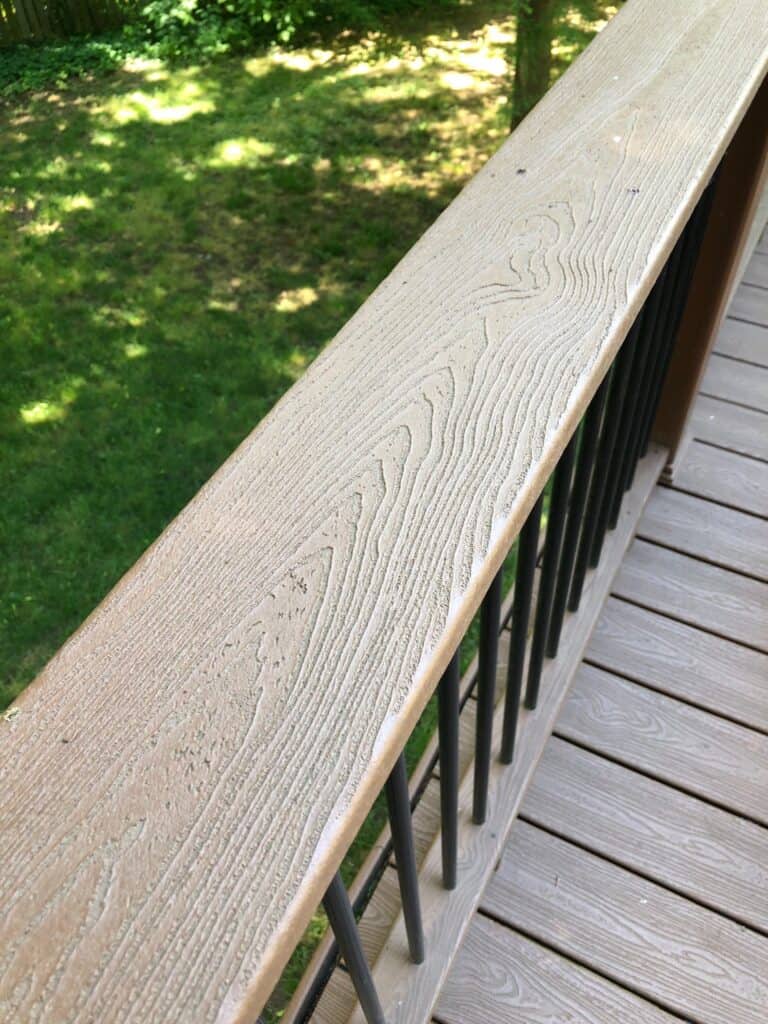 Close-up of a wooden deck railing with textured surface and black metal balusters, overlooking a green backyard, showcasing quality craftsmanship in outdoor living design by DW Construction.