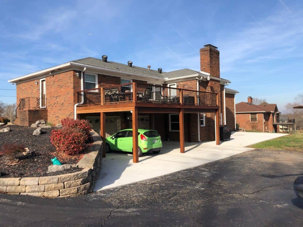 Outdoor living space featuring a wooden deck with railing, brick house, and green car parked beneath, surrounded by landscaped stone walls and shrubs in Nashville, TN.