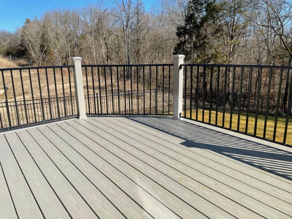 Deck with gray flooring and black railing, surrounded by trees, showcasing outdoor living space design by DW Construction.