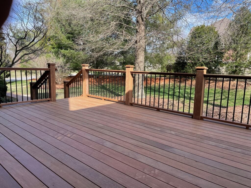 Custom wooden deck with black railing, surrounded by trees and landscaped yard, showcasing outdoor living space design by DW Construction in Nashville.