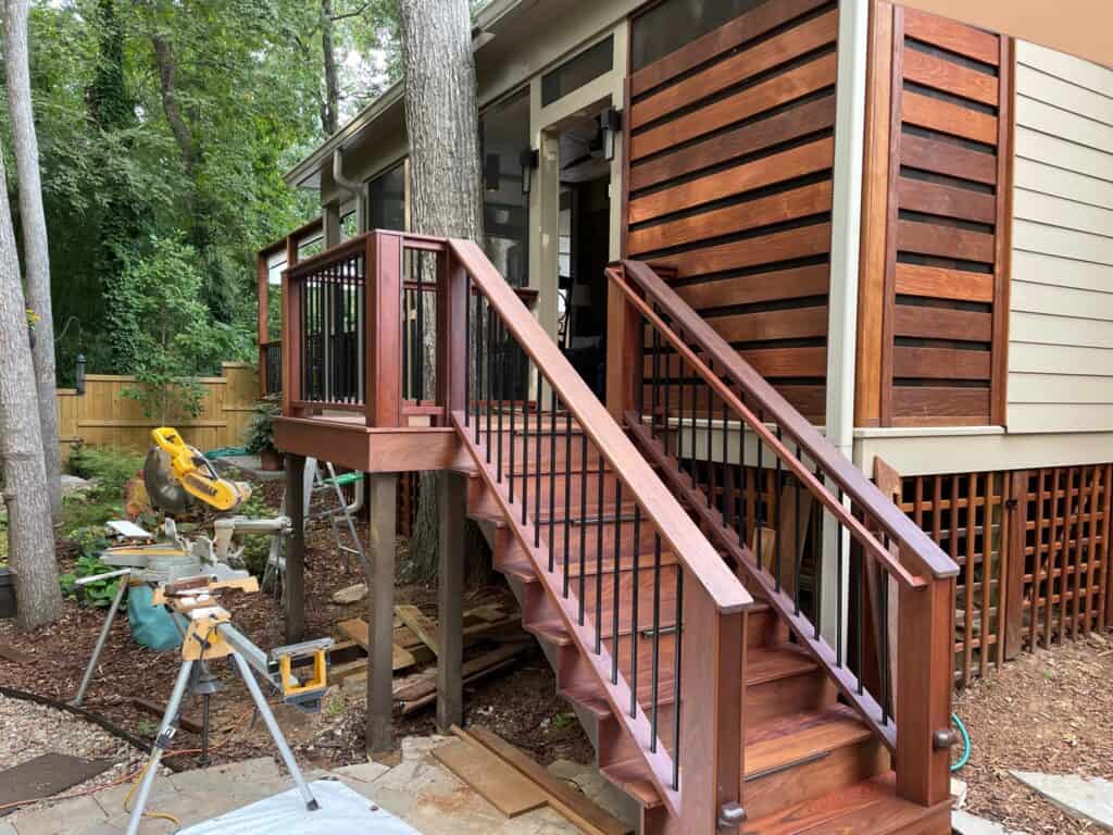 Custom wooden deck and stairs leading to a modern home, surrounded by greenery, showcasing quality craftsmanship in outdoor living design by DW Construction.