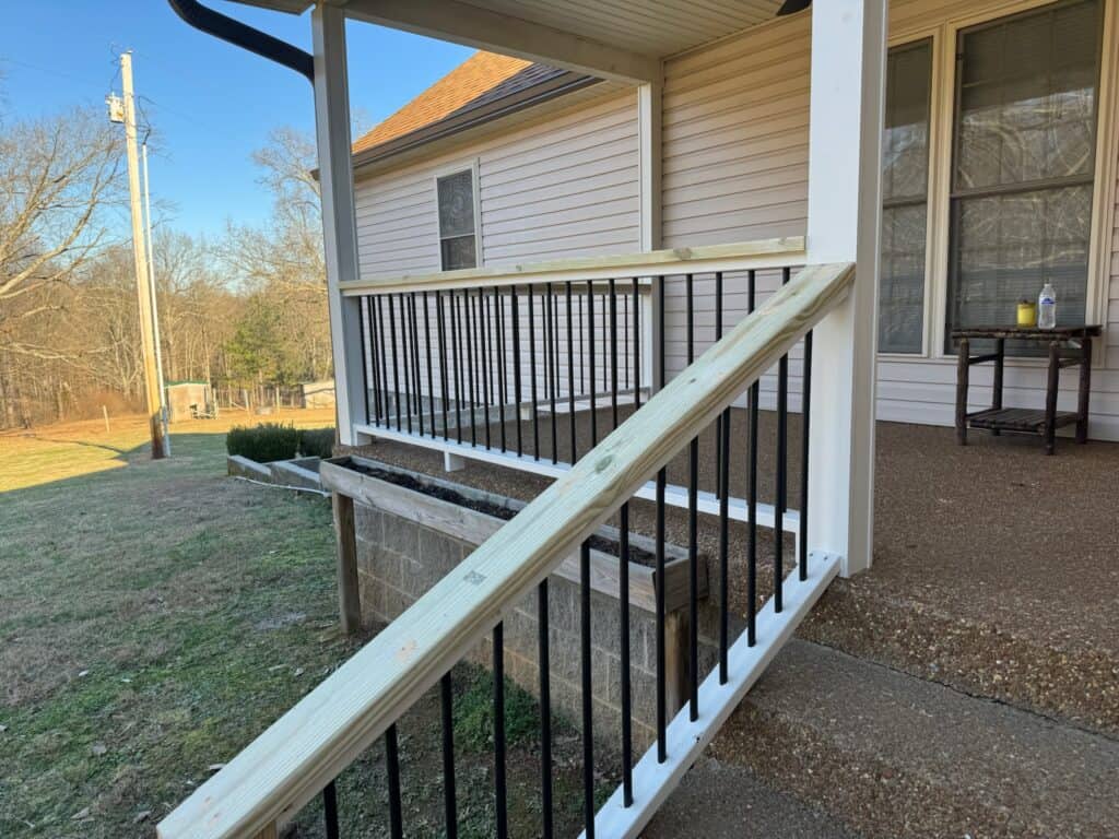 Custom wooden railing on porch with black metal balusters, leading to a well-maintained yard, showcasing DW Construction's outdoor living design expertise in Nashville, TN.