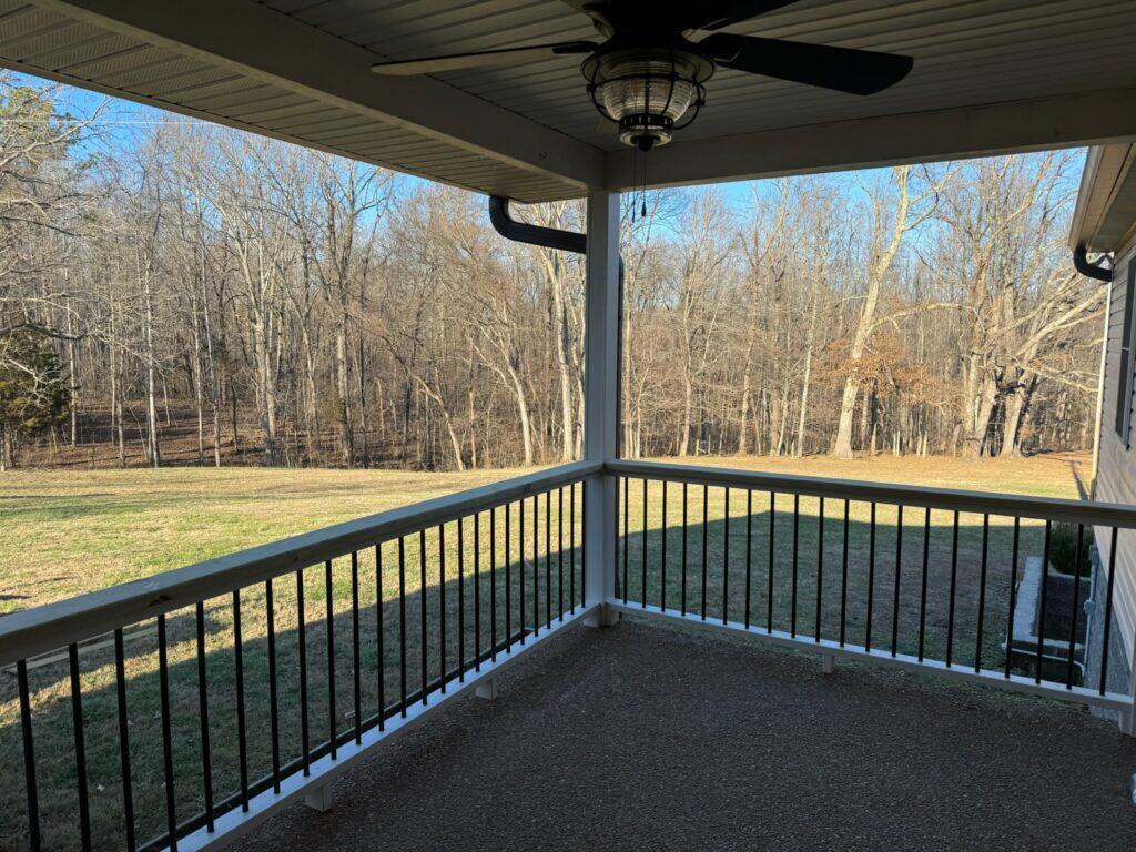 Covered porch with ceiling fan overlooking a grassy yard and wooded area, showcasing outdoor living potential for custom projects by DW Construction in Nashville.