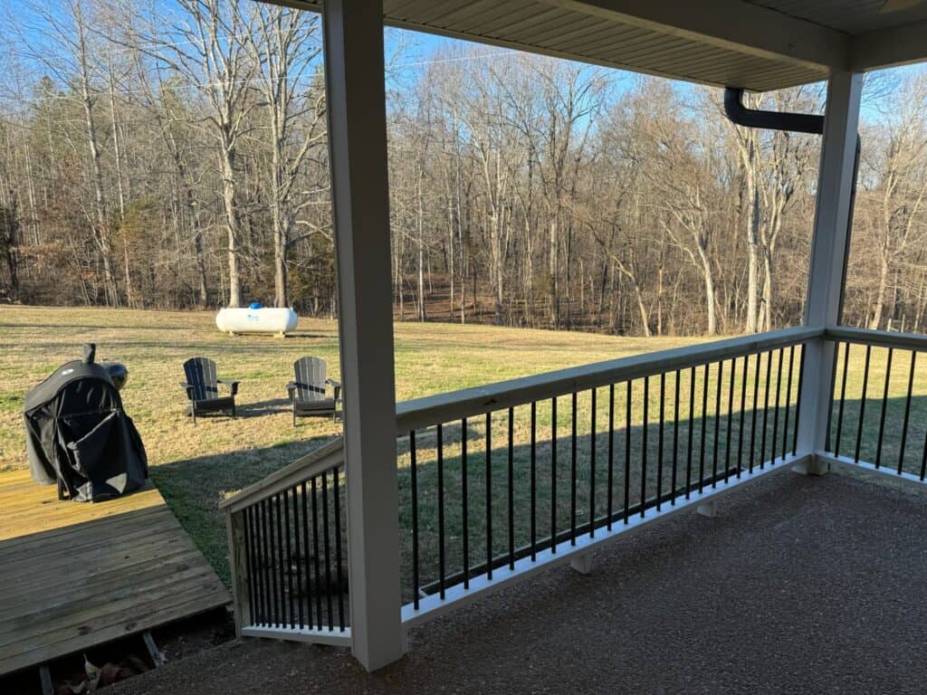 Porch view showcasing a grassy backyard with a grill, Adirondack chairs, and trees, emphasizing outdoor living space design by DW Construction in Nashville.
