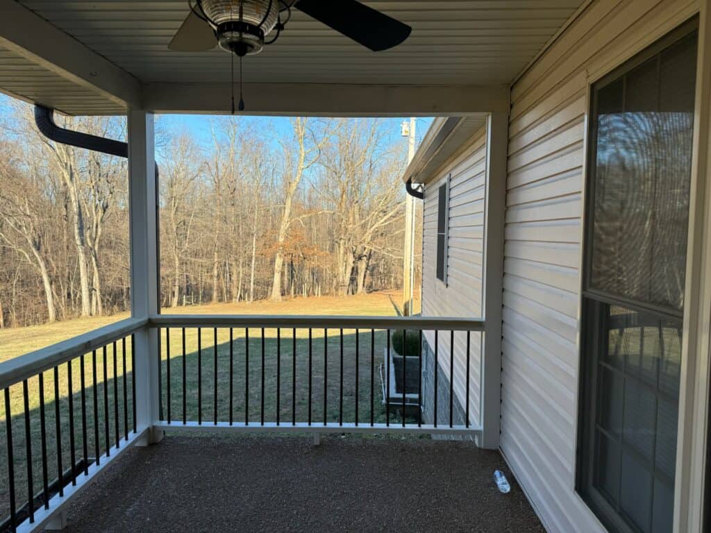 Covered porch view showcasing a ceiling fan and railing, overlooking a grassy area and trees, emphasizing outdoor living space design by DW Construction.