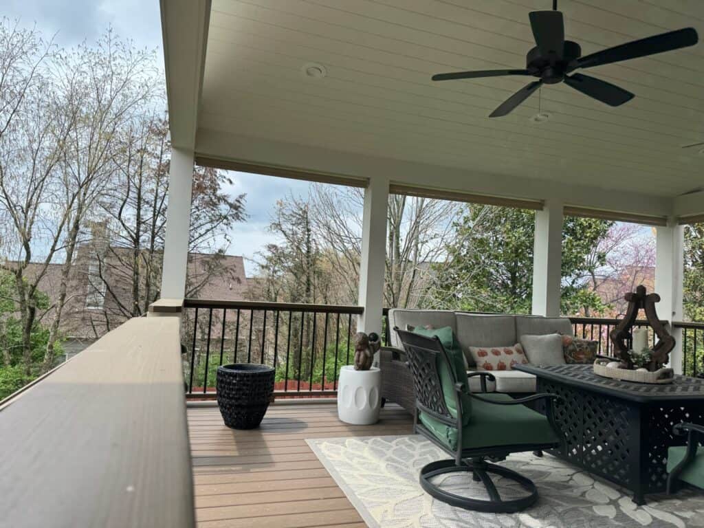 Covered outdoor living space featuring a stylish seating area with a green chair, decorative pillows, a coffee table, and a rug, surrounded by trees and a railing, ideal for relaxation and entertaining in Nashville.