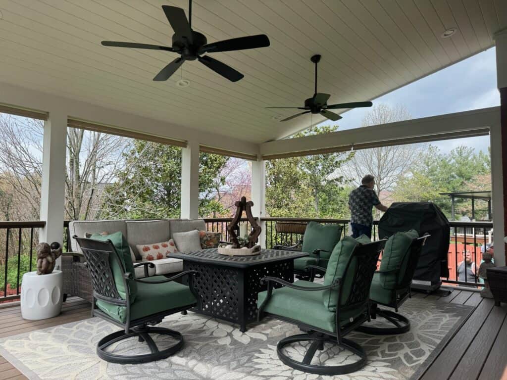 Outdoor living space featuring a comfortable seating area with green chairs, a decorative table, and a grill, surrounded by trees, illustrating DW Construction's custom patio design.