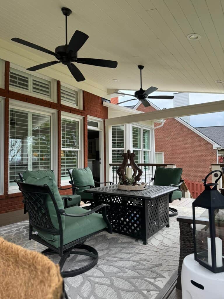 Outdoor living space featuring green cushioned chairs, a black decorative table, and ceiling fans, showcasing a stylish patio design by DW Construction in Nashville, TN.
