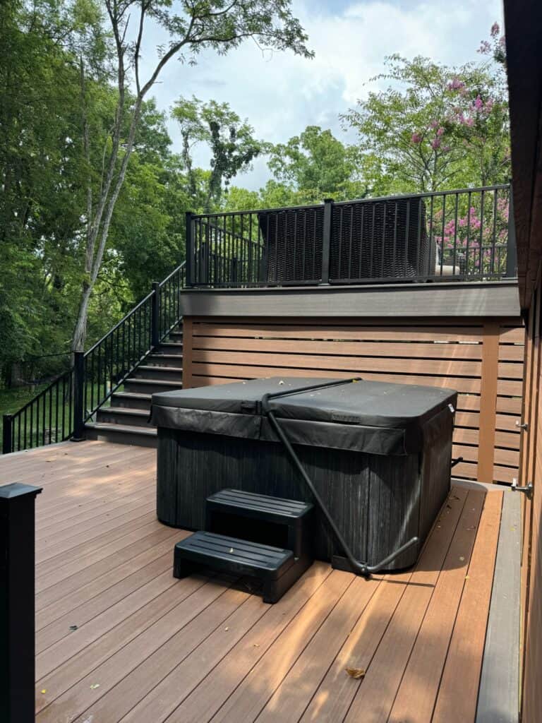 Hot tub on a wooden deck with steps, surrounded by greenery and a railing, showcasing outdoor living space design by DW Construction.