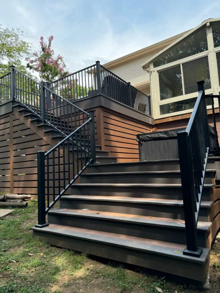 Custom wooden deck with black metal railing and stairs leading to a house, showcasing outdoor living design by DW Construction in Nashville, TN.