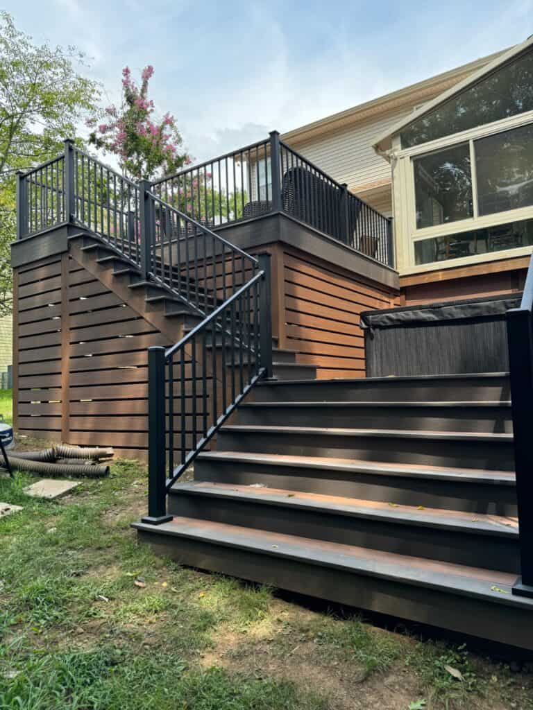 Custom wooden deck with black railings and stairs, surrounded by greenery, showcasing outdoor living design by DW Construction in Nashville.