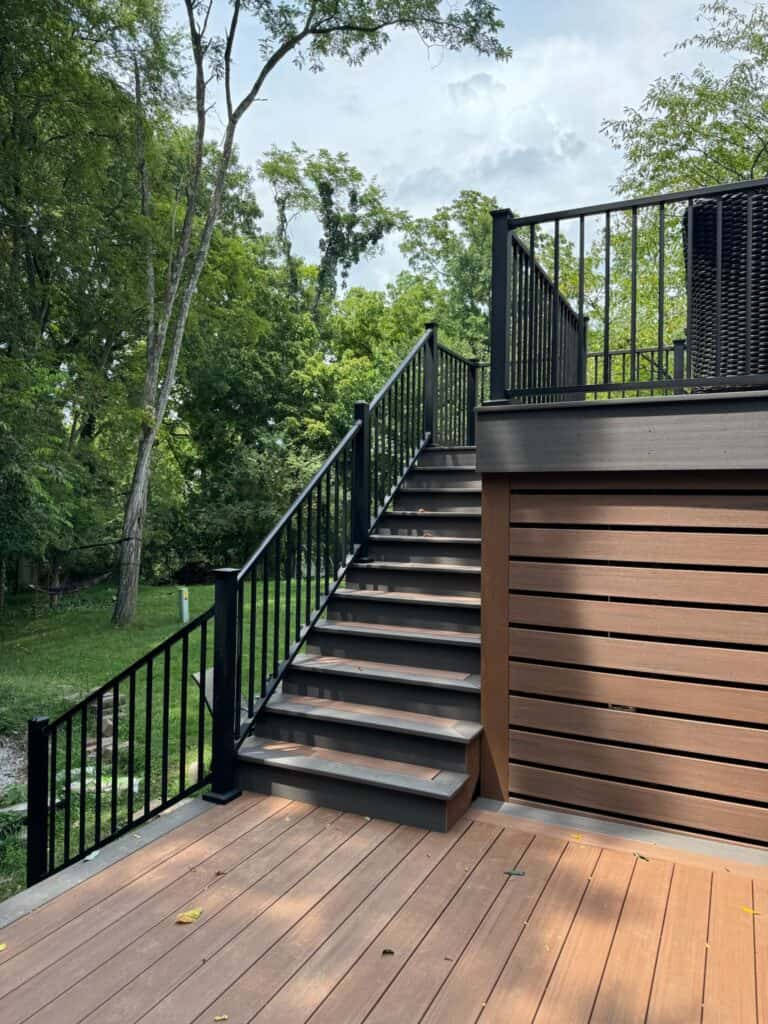 Custom wooden deck with stairs and black railing surrounded by greenery, showcasing outdoor living design by DW Construction in Nashville, TN.