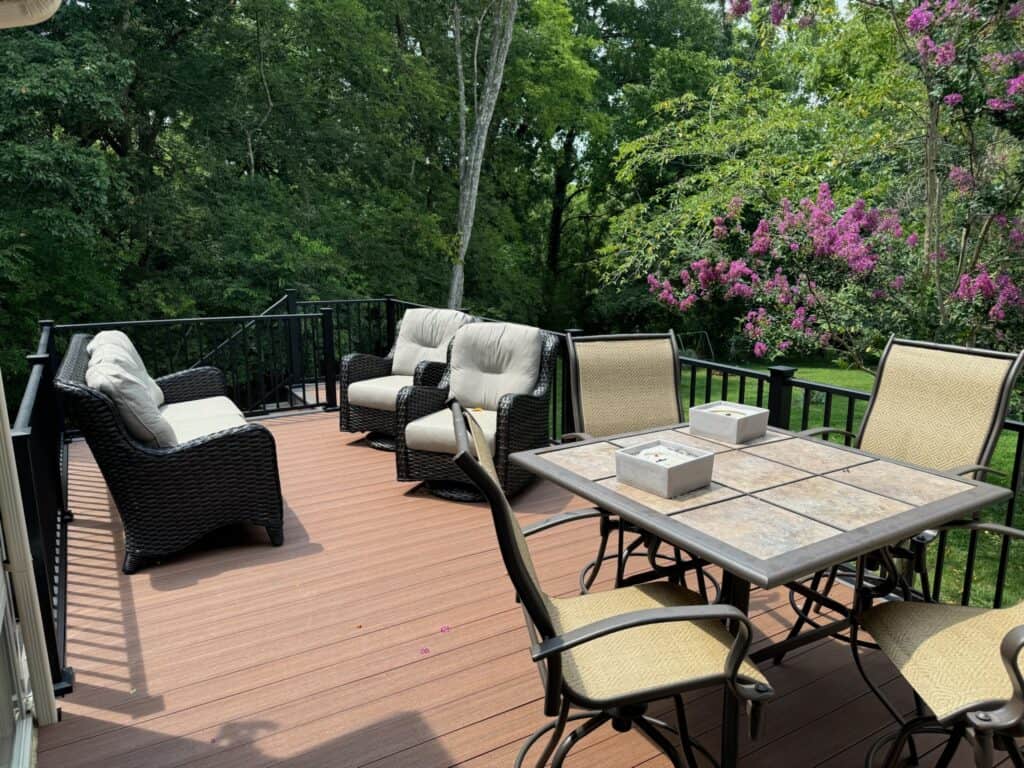 Deck with comfortable seating and a dining table, surrounded by lush greenery and flowering trees, showcasing an outdoor living space designed by DW Construction in Nashville.