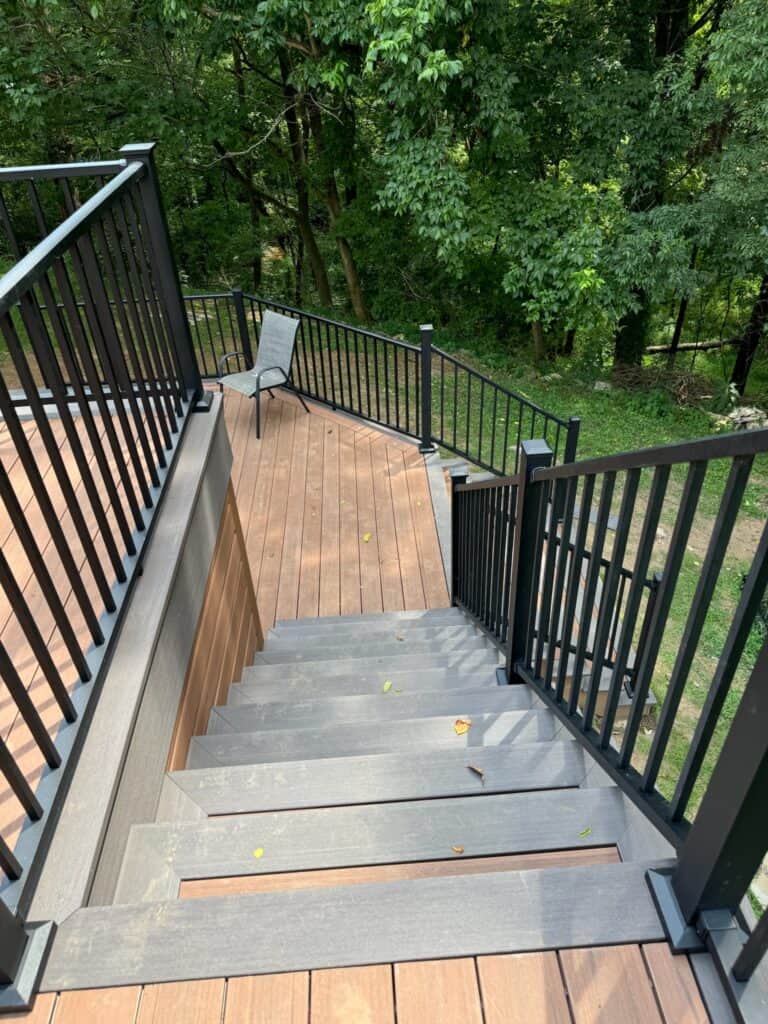 Staircase leading down from a modern deck with black railings, surrounded by lush greenery, showcasing outdoor living design by DW Construction.