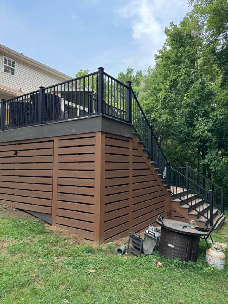 Custom wooden deck with black railings and steps, surrounded by greenery, showcasing outdoor living design by DW Construction in Nashville.