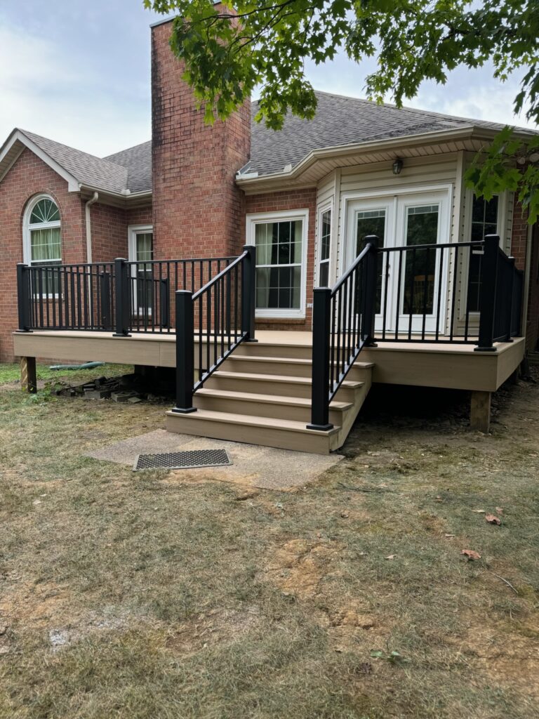 Custom outdoor deck with black railing and steps, adjacent to a brick home, showcasing DW Construction's craftsmanship in outdoor living spaces.